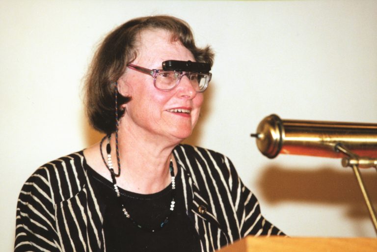 Frances Cutler, ancienne présidente, Conseil d’administration national d’INCA, porte des télescopes attachés à ses lunettes afin de voir la réaction du public pendant qu’elle parle sur le podium.